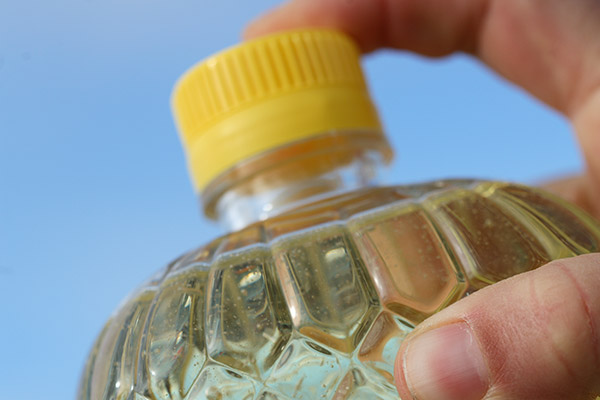 A hand holding a canola oil bottle with a yellow lid, partially visible with one finger resting on it