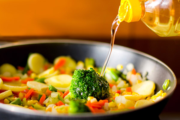 Drizzling canola oil over a vegetable dish with broccoli