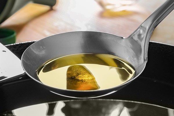 A ladle with liquid, possibly oil, resting on a black surface, reflecting an inverted image of a kitchen.