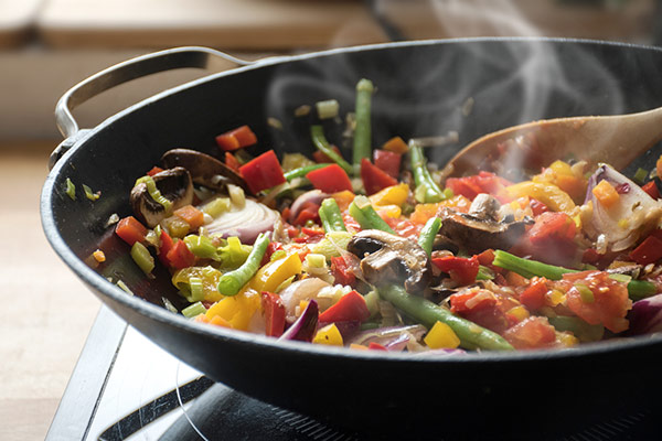 A variety of vegetables, including bell peppers, green beans, onions, and mushrooms, being sautéed in a pan on a stove.