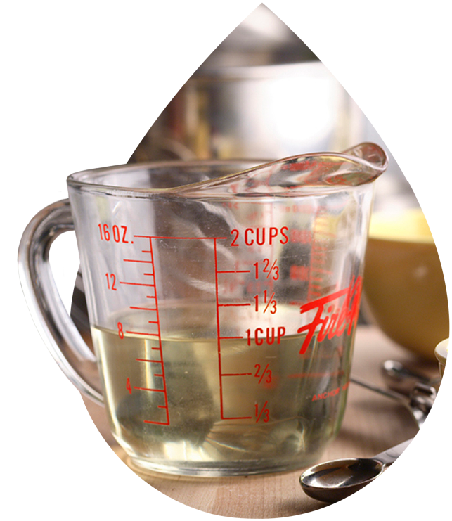 Glass measuring cup filled with liquid, showing measurements in ounces and cups, placed on a kitchen counter with utensils.